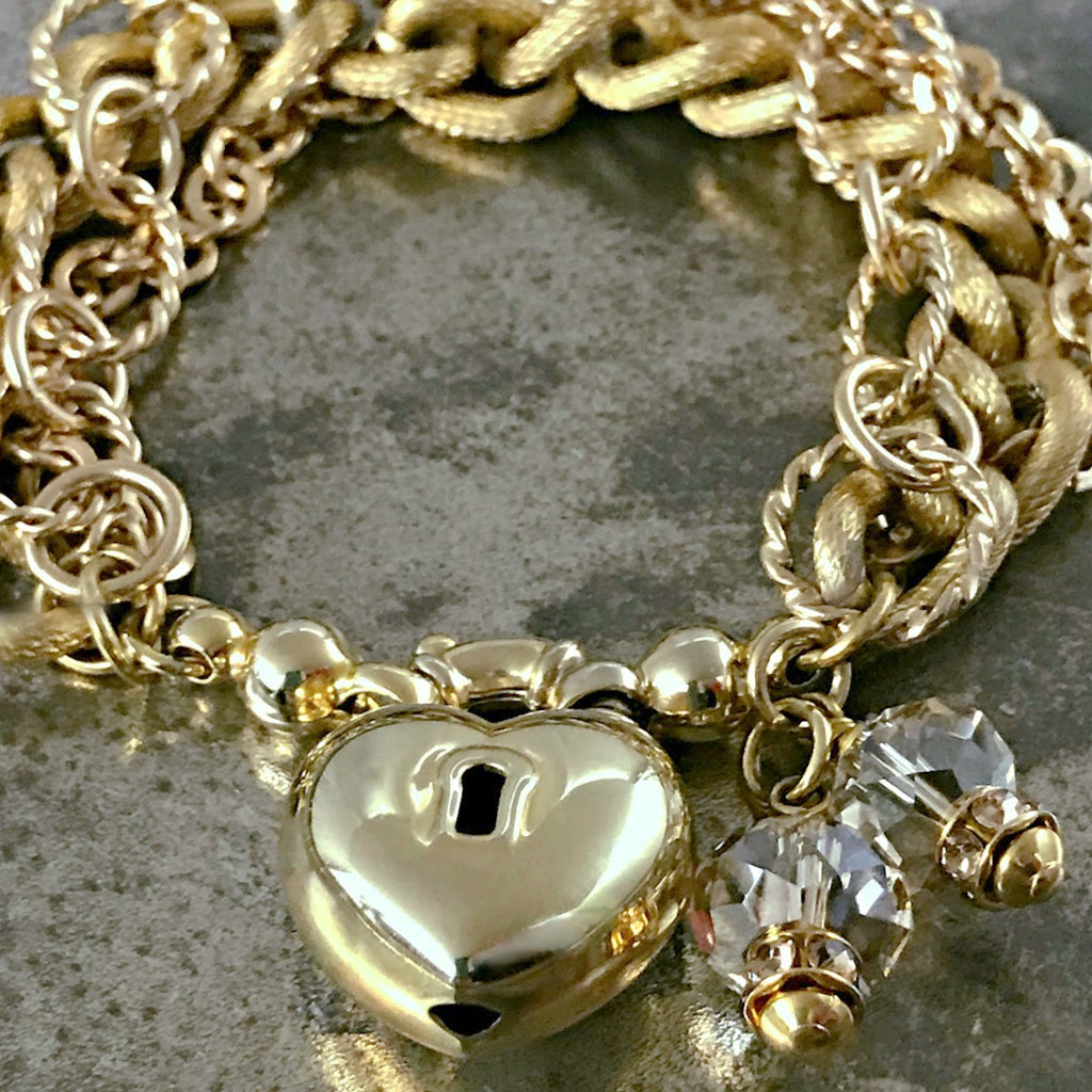 ​​​The soft gold color of this Suzie Q Studio one-o​f​-a-kind bracelet, along with the sparkle of Swarovski crystals, three styles of chain and unusual heart-shaped focal closure, provides an elegant, show-stopper look