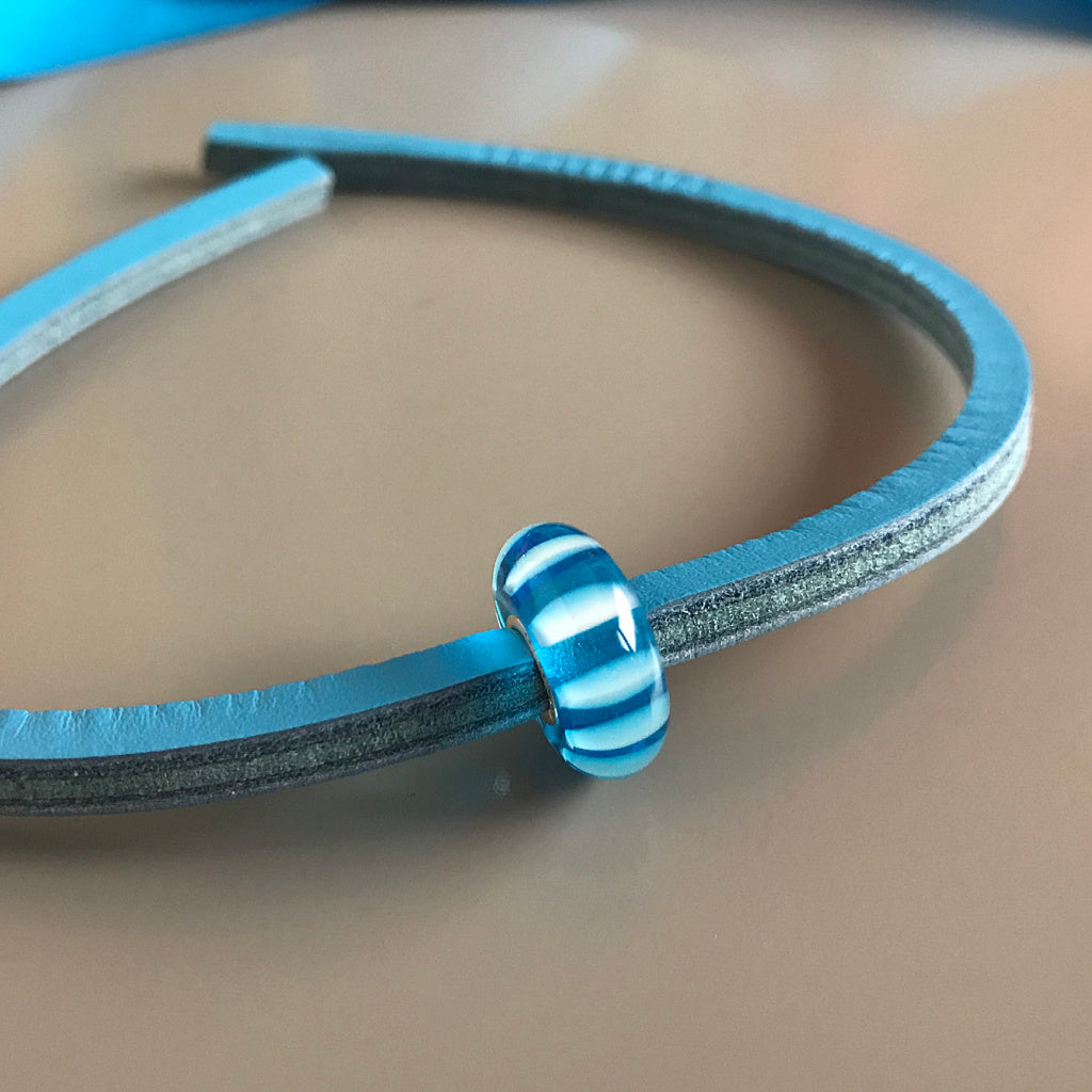 Trollbeads UNIQUES are one-of-a-kind glass beads handmade individually by 100% artisan-owned workshops in Tibet, India, Malawi and Lithuania. This Suzie Q Studio bright blue striped UNIQUES glass bead also includes a colour-coordinated leather bracelet.