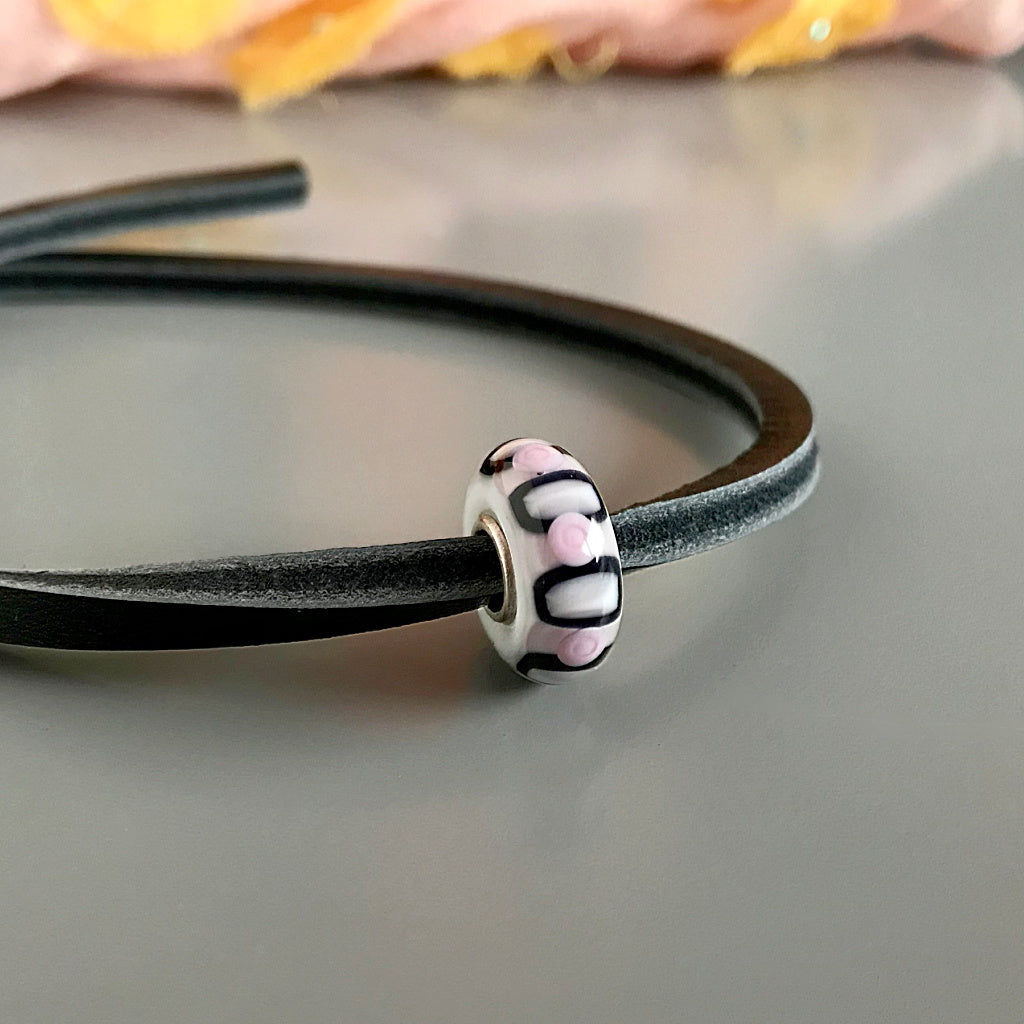 Trollbeads UNIQUES are one-of-a-kind glass beads handmade individually by 100% artisan-owned workshops. This Suzie Q Studio UNIQUES glass bead has a retro-style design in the striking colour-combo of pale pink, black and white!