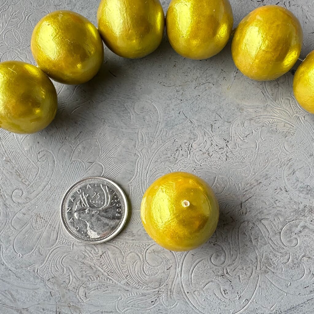 One strand of 6, 24mm round, chartreuse coloured, cotton pearl beads with a pearlized, lightweight, textured finish, shown on an embossed grey background, from Suzie Q Studio.
