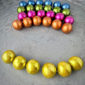 One strand of 6, 24mm round, chartreuse coloured, cotton pearl beads with a pearlized, lightweight, textured finish, shown on an embossed grey background, from Suzie Q Studio.