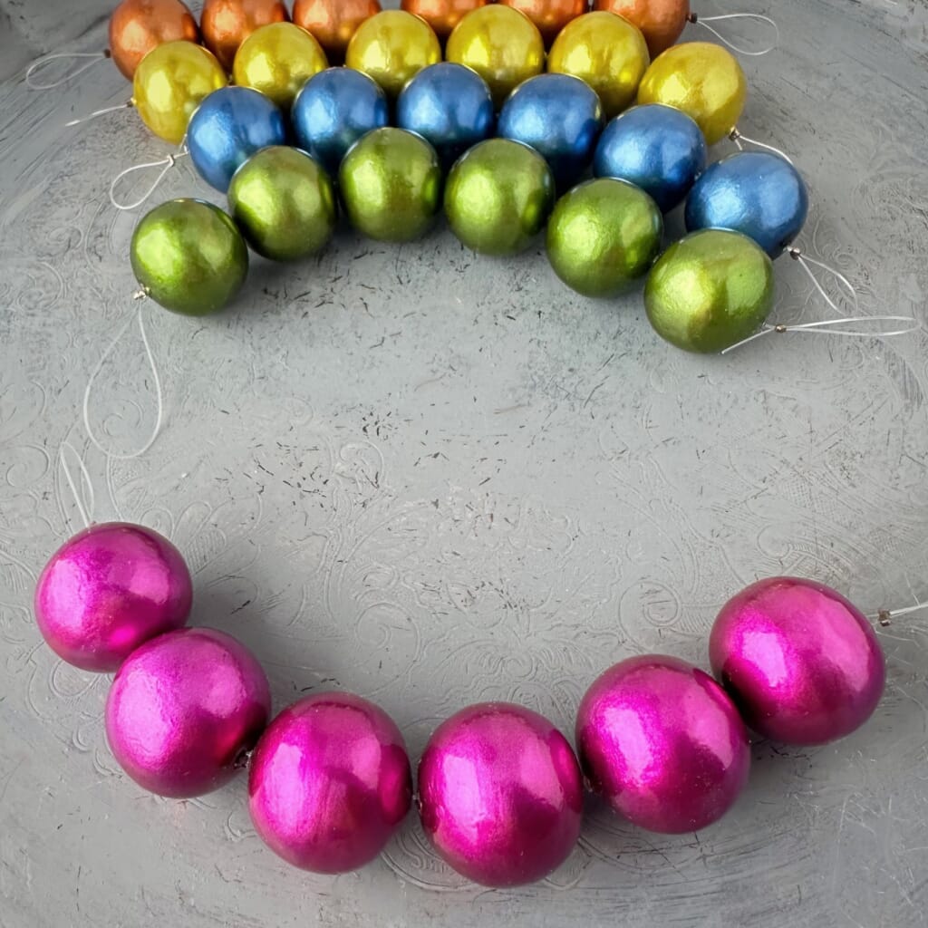 One strand of 6, 24mm round, fuchsia coloured, cotton pearl beads with pearlized finish, lightweight and textured, shown on a grey background, from Suzie Q Studio.