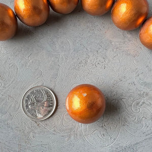 24mm orange cotton pearl bead with glossy pearl coating, lightweight and round, next to a Canadian quarter to show scale, available at Suzie Q Studio.