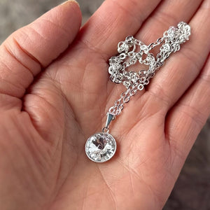 Swarovski crystal necklace, with round, "rivoli” stone pendant, in crystal FB / Foil Back finish, on silver-plated chain, shown in hand to show scale.