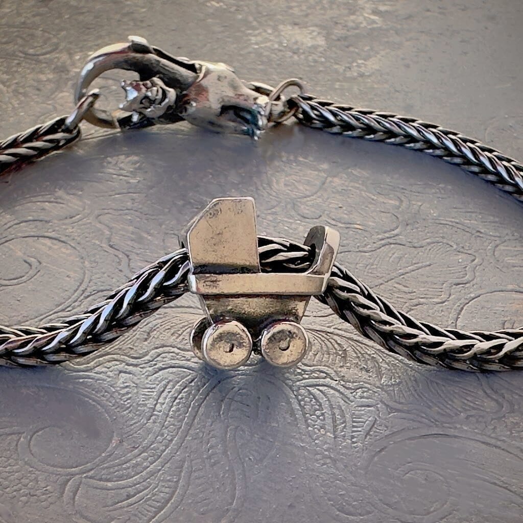 Trollbeads 30th Anniversary, sterling silver bead called, BEGINNING OF LIFE, featuring an adorable baby carriage,  is shown on a sterling silver bracelet, with lock. Shop online for one-of-a-kind treasures at Suzie Q Studio.