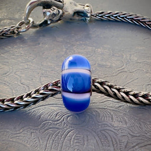 LE Trollbeads 30th Anniversary, glass bead, in white and various tones of blue, called, STRIPE OF THE SEA, shown on a sterling silver bracelet, with lock. Shop online for one-of-a-kind treasures at Suzie Q Studio.