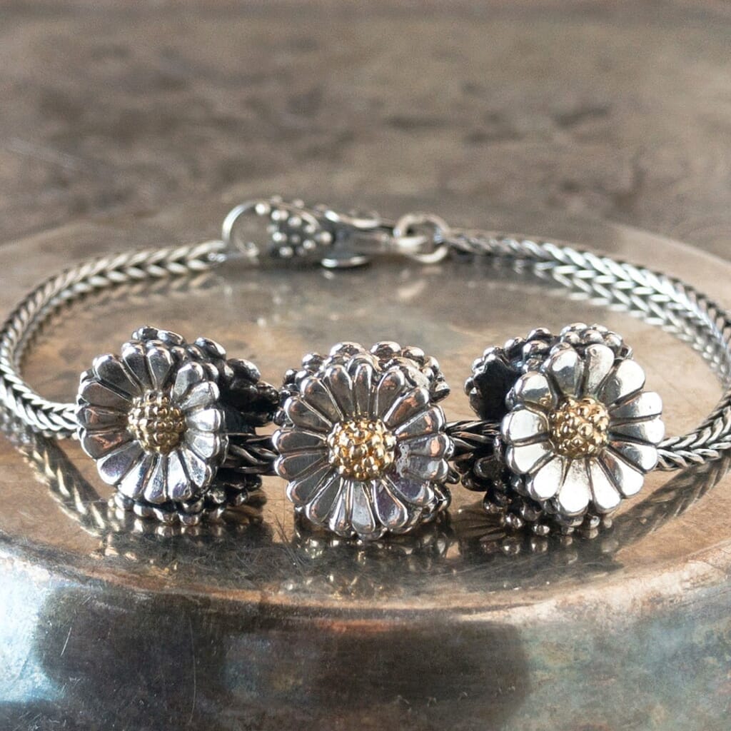 3 sterling silver & 18 karat gold Trollbeads DAISY beads, each bead showing 3 different sides, on a sterling silver Trollbeads bracelet.