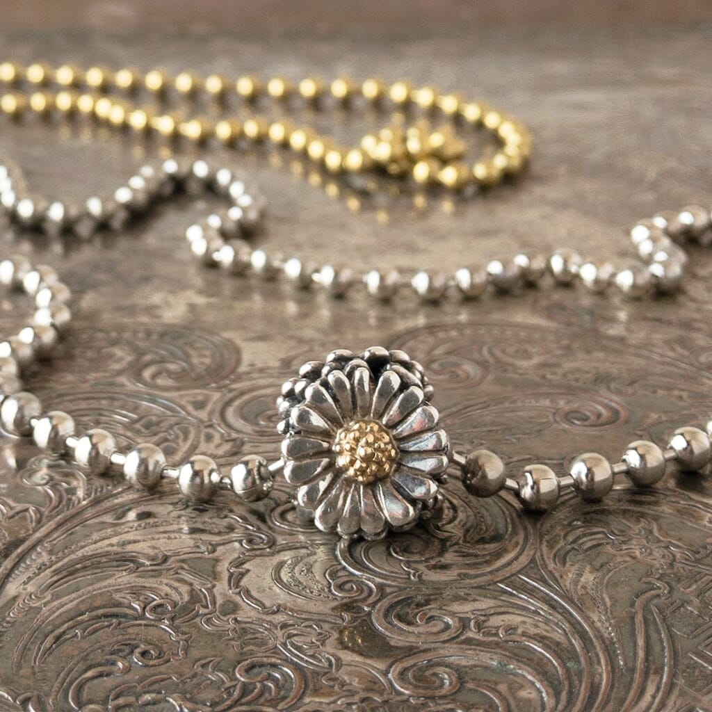Trollbeads sterling & 18 karat DAISY bead, shown with a gold tone & silver tone ball chain, displayed on a tray.