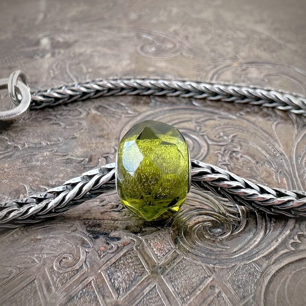 Trollbeads, retired, GREEN PRISM, faceted, glass bead, which is shown on a sterling silver Trollbeads bracelet, with a clasp, on an embossed background, and is available at Suzie Q Studio dot com.