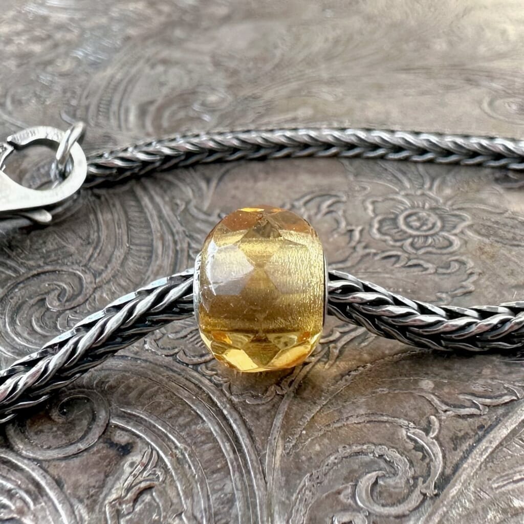 Trollbeads, retired, YELLOW PRISM, faceted, glass bead, which is shown on a sterling silver Trollbeads bracelet, with a clasp, on an embossed background, and is available at Suzie Q Studio dot com.