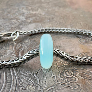 Trollbeads, retired, limited edition, TURQUOISE AGATE stone bead, shown on a sterling silver chain bracelet and clasp, shown on an embossed background -- Front View.