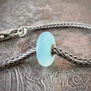 Trollbeads, retired, limited edition, TURQUOISE AGATE stone bead, shown on a sterling silver chain bracelet and clasp, shown on an embossed background -- Side View.