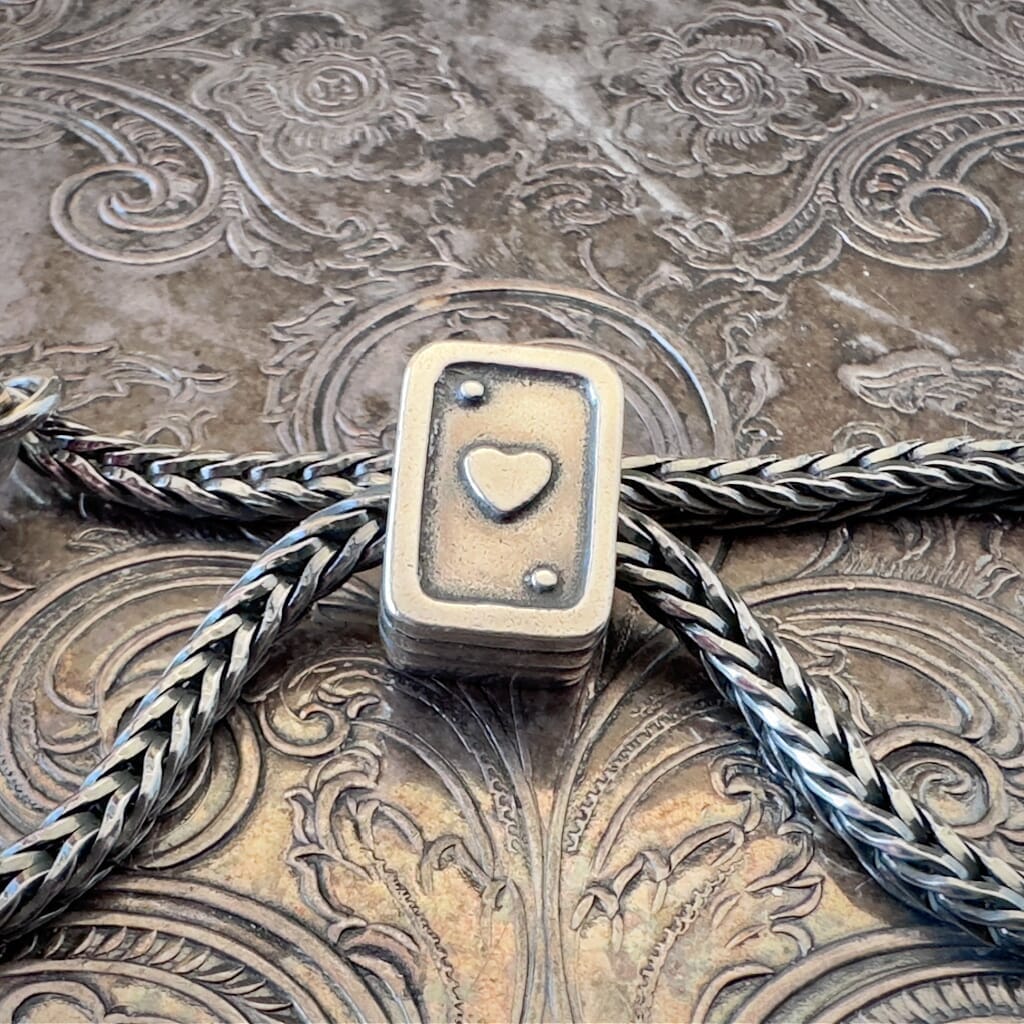 Trollbeads, retired, sterling silver, PLAYING CARDS bead, showing the front side with a heart, on a sterling silver Trollbeads bracelet,  on an embossed background, available at Suzie Q Studio dot com.
