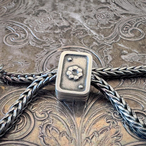 Trollbeads, retired, sterling silver, PLAYING CARDS bead, showing the reverse side with an embossed flower, shown on a sterling silver Trollbeads bracelet, on an embossed background, available at Suzie Q Studio dot com.