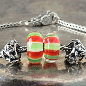 Two versions of glass Caprese Trollbead, with alternating stripes of green, white and red, on a Trollbeads silver bracelet.