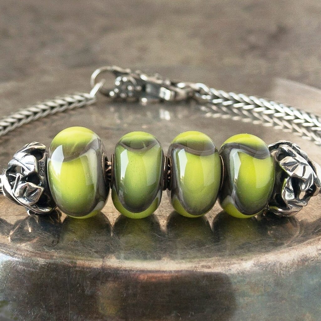 Four versions of glass Green Armadillo Trollbead, with lime and charcoal scale-like design, on Trollbeads silver bracelet.