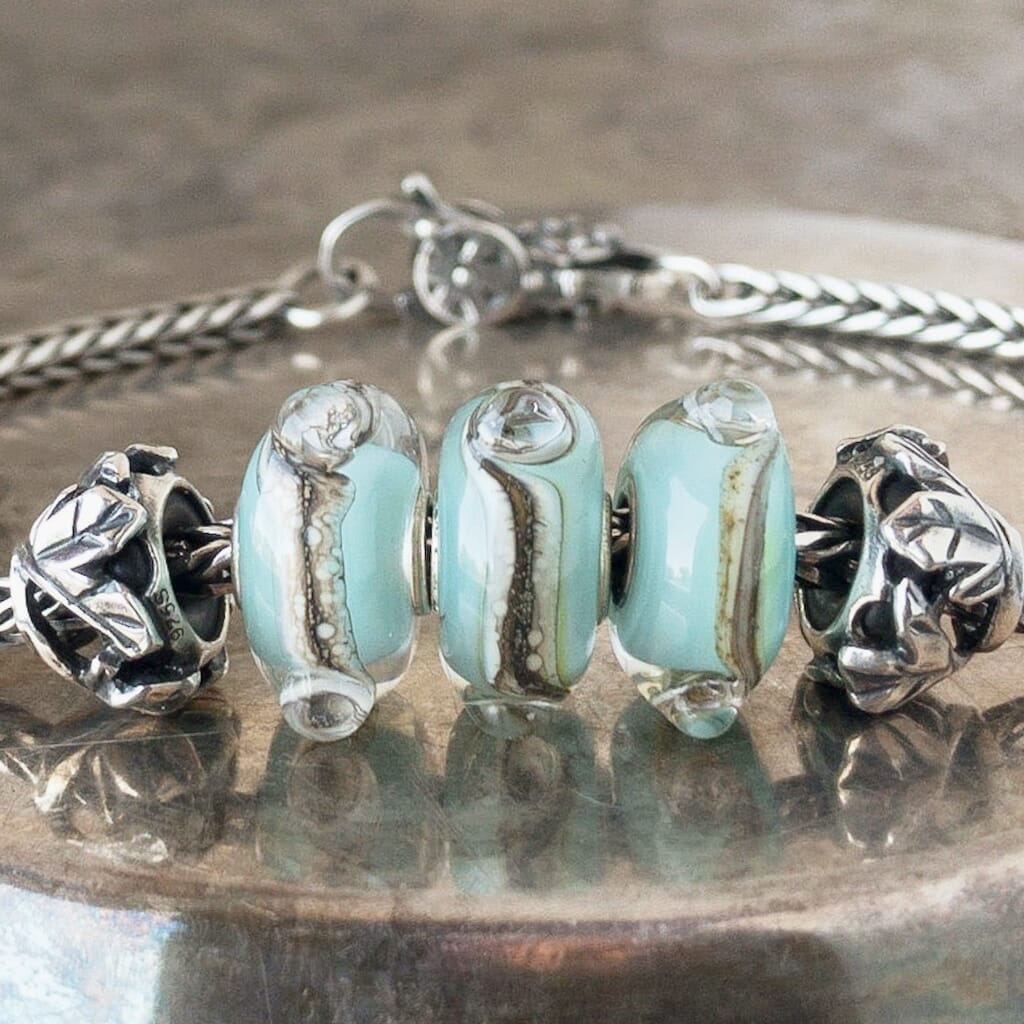 Three versions of glass TRACES Trollbead, with swirls of cream and brown on a baby blue base, on a Trollbeads silver bracelet.