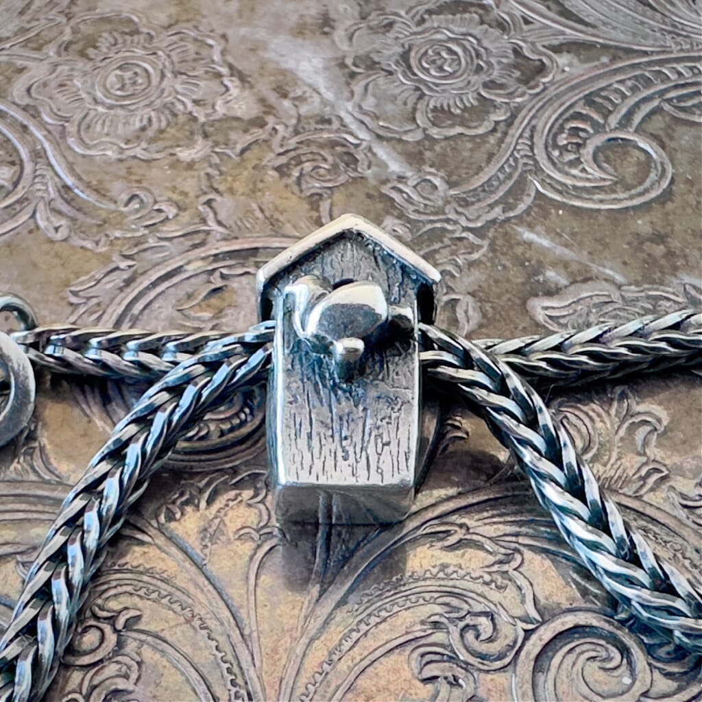 Trollbeads, retired, sterling silver, BIRDHOUSE bead, showing the front side, on a sterling silver Trollbeads bracelet, on an embossed background, available at Suzie Q Studio dot com.