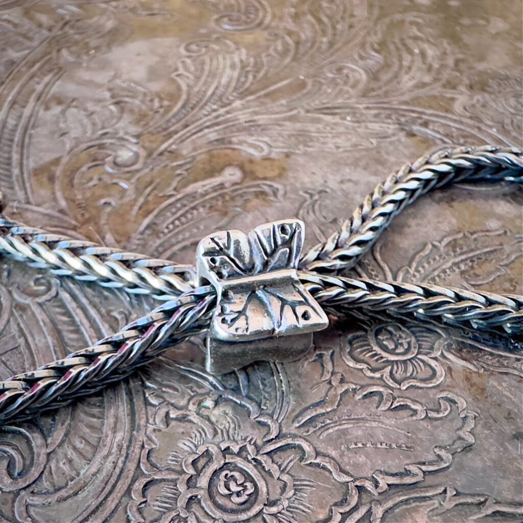 Trollbeads, retired, sterling silver, BUTTERFLY bead, shown on a sterling silver Trollbeads bracelet, on an embossed background, and available at Suzie Q Studio dot com.