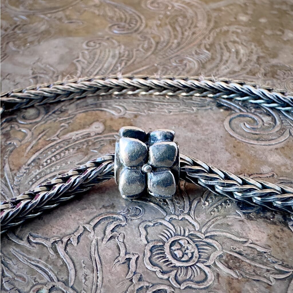 Trollbeads, retired, sterling silver, FLOWERS bead, shown on a sterling silver Trollbeads bracelet, on an embossed background, and available at Suzie Q Studio dot com.