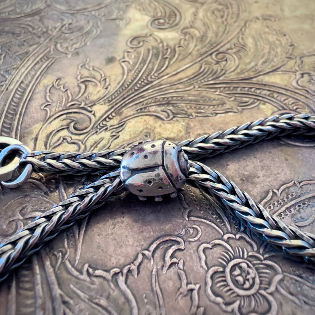 Trollbeads, retired, sterling silver, LADY BUG bead, shown on a sterling silver Trollbeads bracelet, with a clasp, on an embossed background, and available at Suzie Q Studio dot com.