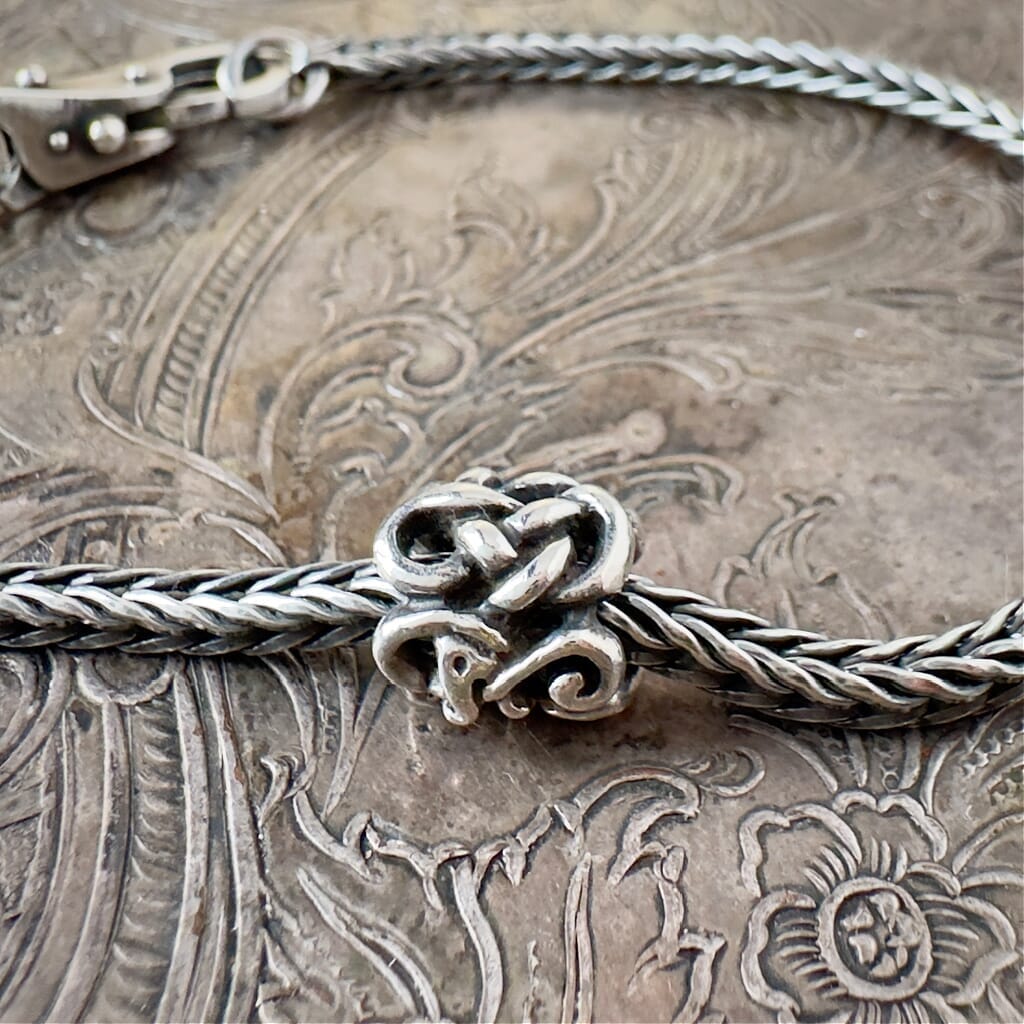 Trollbeads, retired, sterling silver, THE MIDGARD SERPENT bead, shown on a sterling silver Trollbeads bracelet, with a clasp, on an embossed background, and available at Suzie Q Studio dot com.