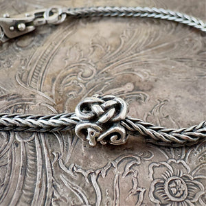 Trollbeads, retired, sterling silver, THE MIDGARD SERPENT bead, shown on a sterling silver Trollbeads bracelet, with a clasp, on an embossed background, and available at Suzie Q Studio dot com.