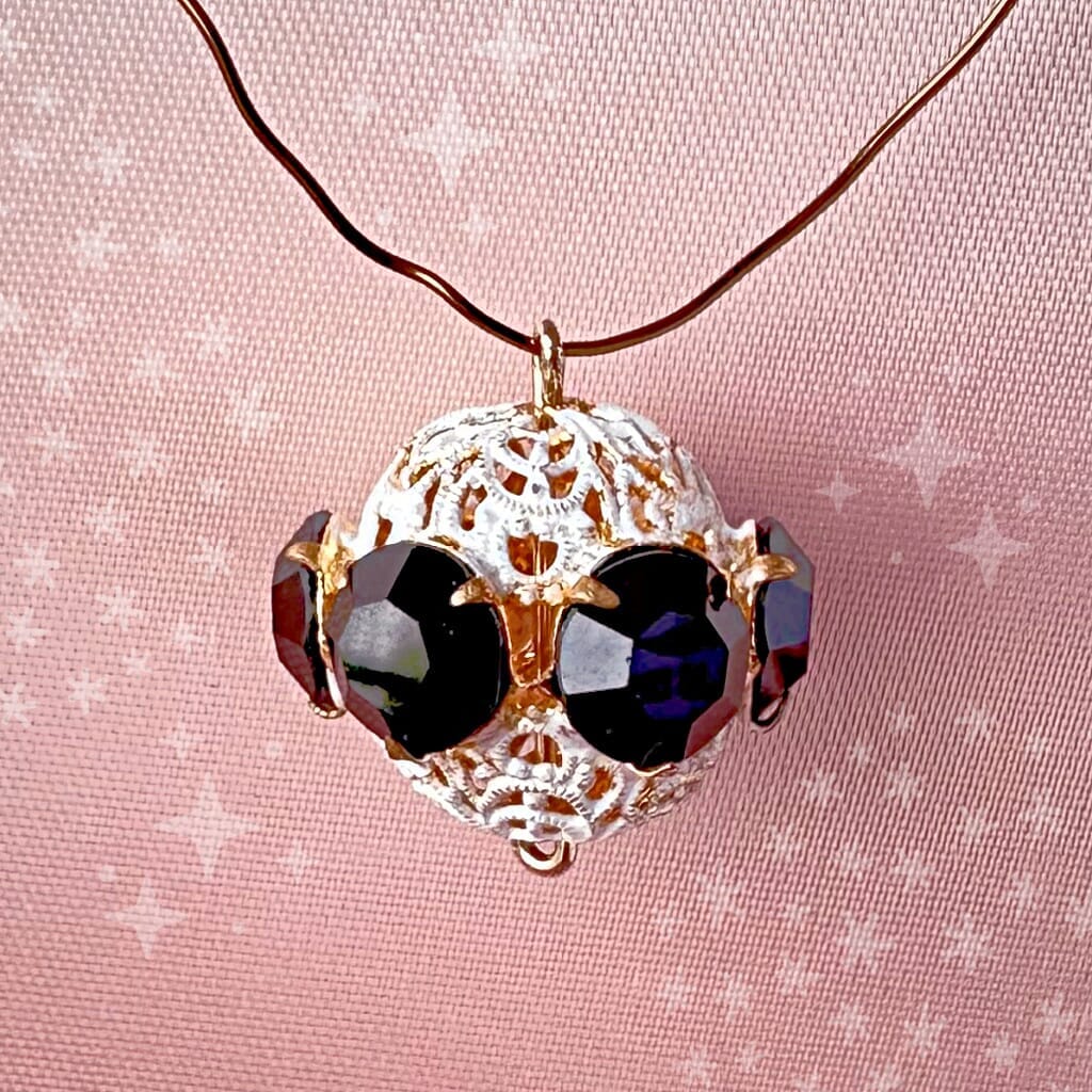 Vintage, opaque jet black and white enamelled, Swarovski rhinestone bead ball on a pink background.