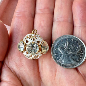 Vintage, crystal-coloured, Swarovski rhinestone bead ball next to a Canadian quarter coin on a hand for size comparison.