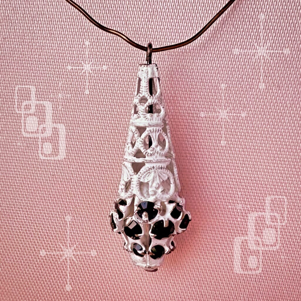 Vintage, Swarovski rhinestone, teardrop-shaped, white filigree bead/charm with jet black-coloured stones on a pink background.