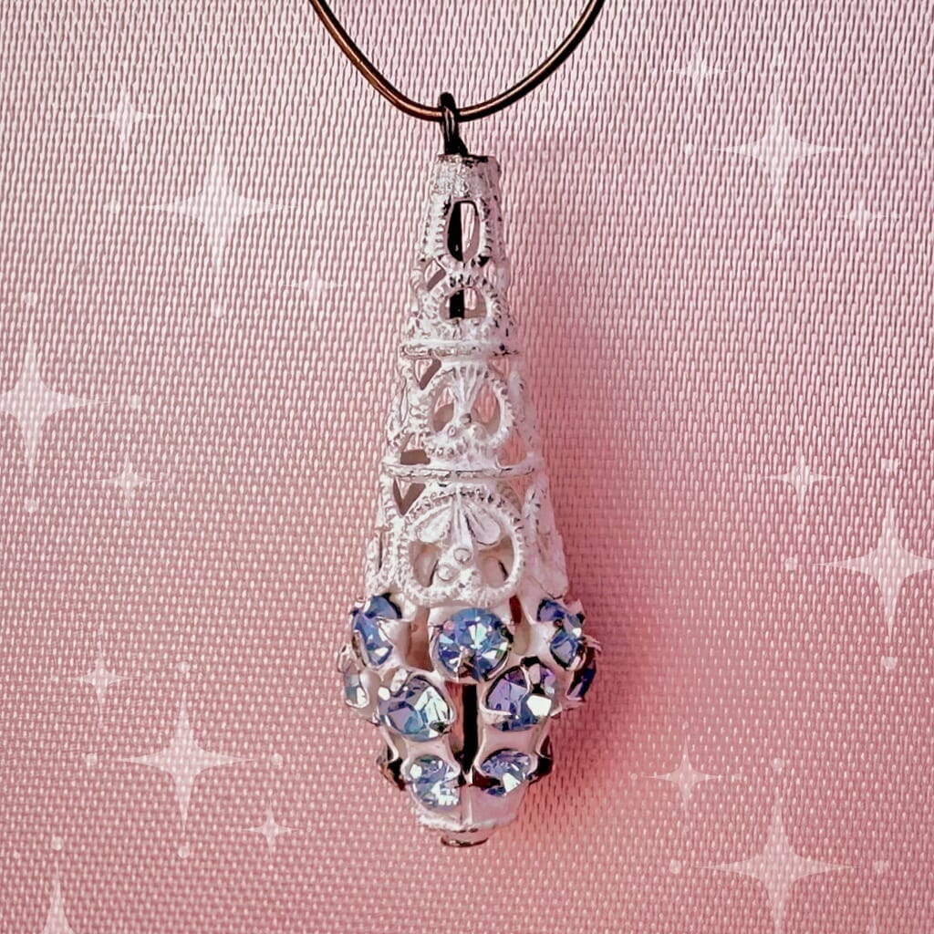 Vintage, Swarovski rhinestone, teardrop-shaped, white filigree bead / charm with light sapphire-coloured stones on a pink background.