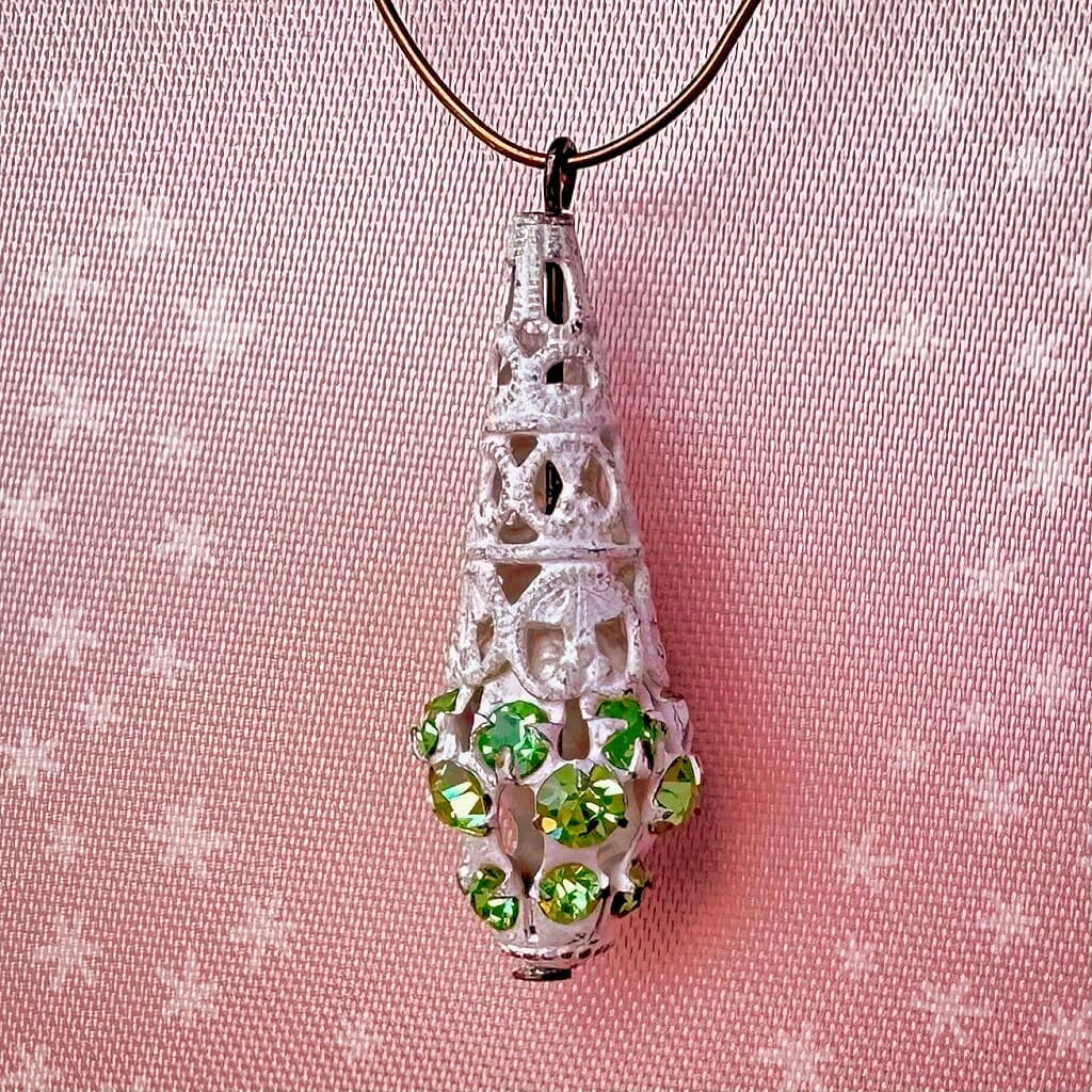 Vintage, Swarovski rhinestone, teardrop,-shaped, white filigree bead ball charm with peridot-coloured stones on a pink background.