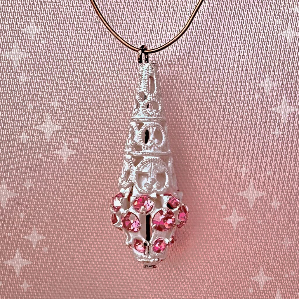 Vintage, Swarovski rhinestone, teardrop-shaped, white filigree bead / charm with rose pink stones on a pink background.