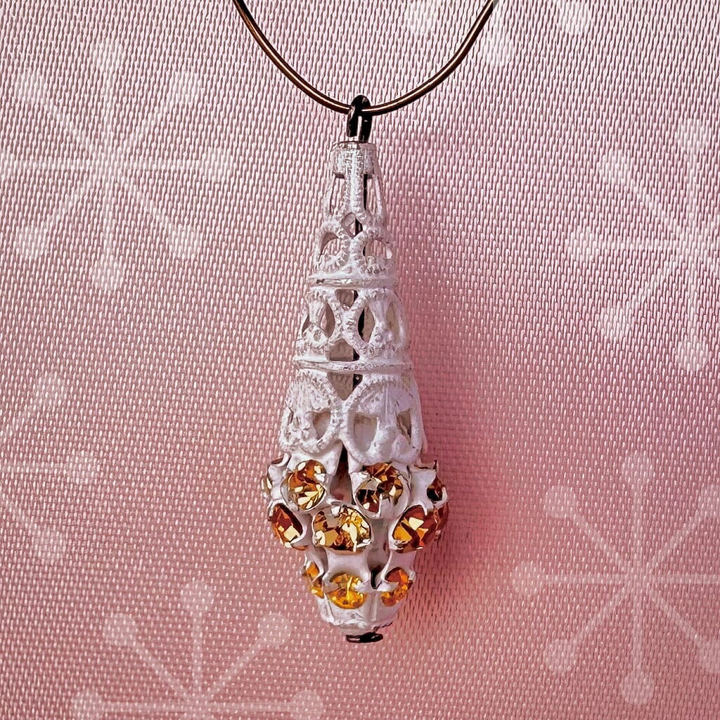 Vintage, Swarovski rhinestone, teardrop-shaped, white filigree bead / charm with topaz and light topaz-coloured stones on a pink background.