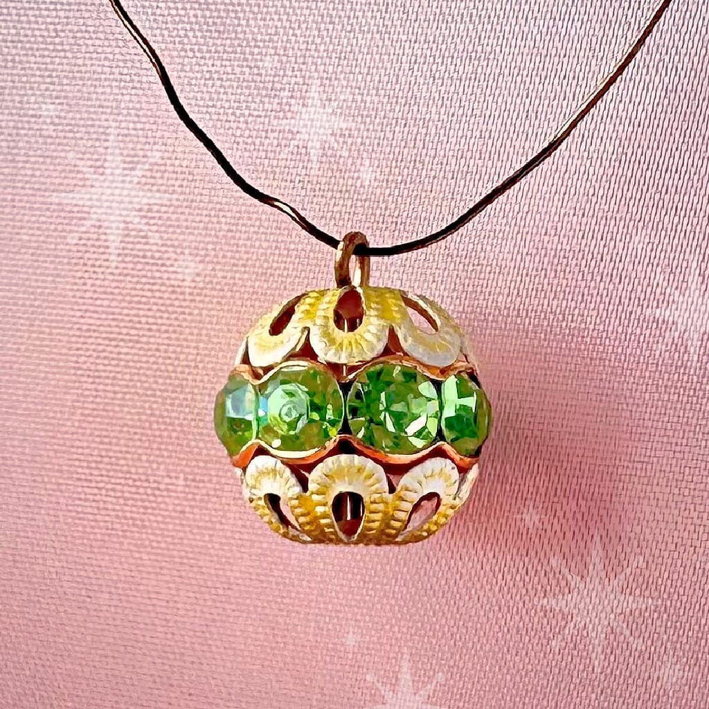 Vintage, peridot-coloured, Swarovski rhinestone bead ball  charm on a pink background.