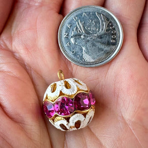Vintage, fuchsia-coloured, Swarovski rhinestone bead ball next to a Canadian quarter coin on a hand for size comparison.
