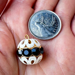 Vintage, jet black-coloured, Swarovski rhinestone bead ball next to a Canadian quarter coin on a hand for size comparison.