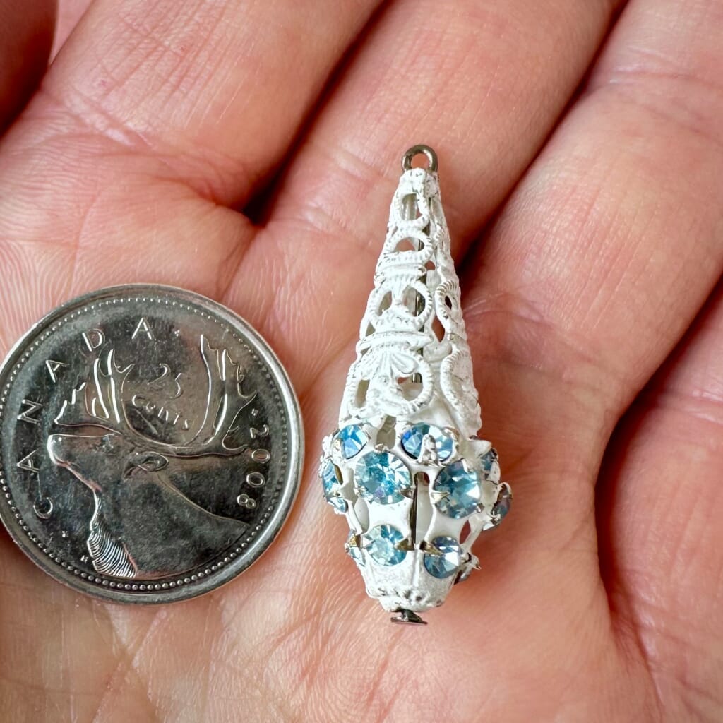 Vintage, Swarovski rhinestone, teardrop-shaped, white filigree bead / charm with light sapphire-coloured stones on a pink background.