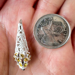 Vintage, light topaz-coloured, Swarovski rhinestone, filigree, teardrop bead ball next to a Canadian quarter coin on a hand for size comparison.