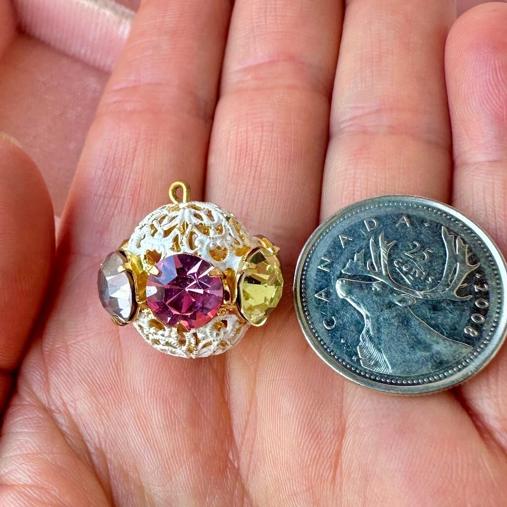 Vintage, multi-coloured, Swarovski rhinestone bead ball next to a Canadian quarter coin on a hand for size comparison.