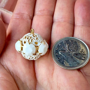 Vintage, opaque white-coloured, Swarovski rhinestone bead ball next to a Canadian quarter coin on a hand for size comparison.