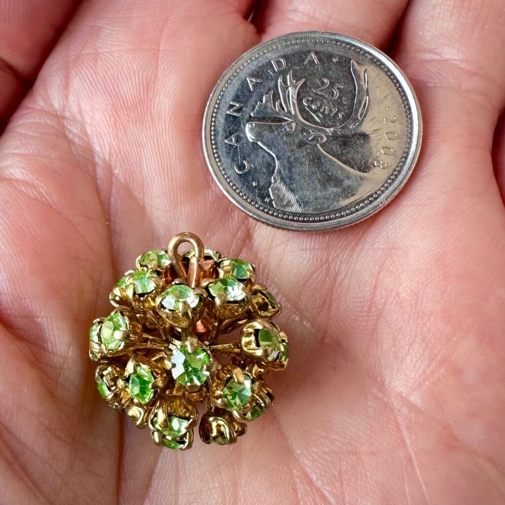 Vintage, Swarovski rhinestone bead ball, peridot-coloured stones and gold toned metal, on a pink background.