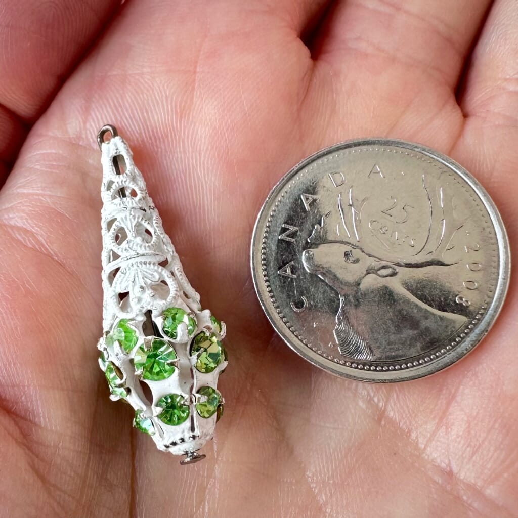 Vintage, Swarovski rhinestone, teardrop,-shaped, white filigree bead ball charm with peridot-coloured stones on a pink background.