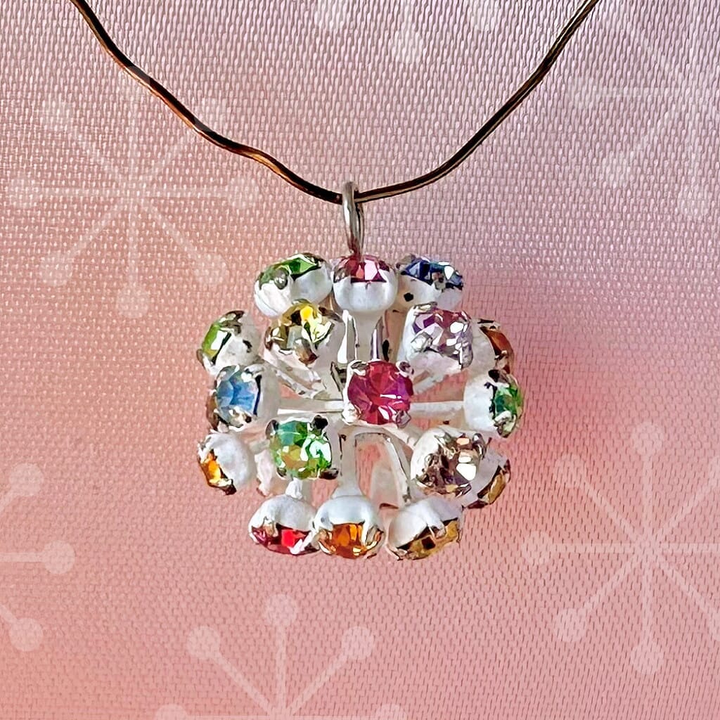 Vintage, Swarovski rhinestone bead ball, with multi-coloured stones and white metal, on a pink background.