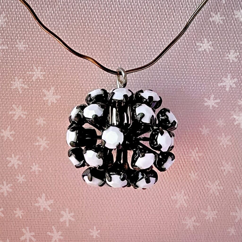 Vintage, Swarovski rhinestone bead ball, with opaque white-coloured stones and black metal, on a pink background.