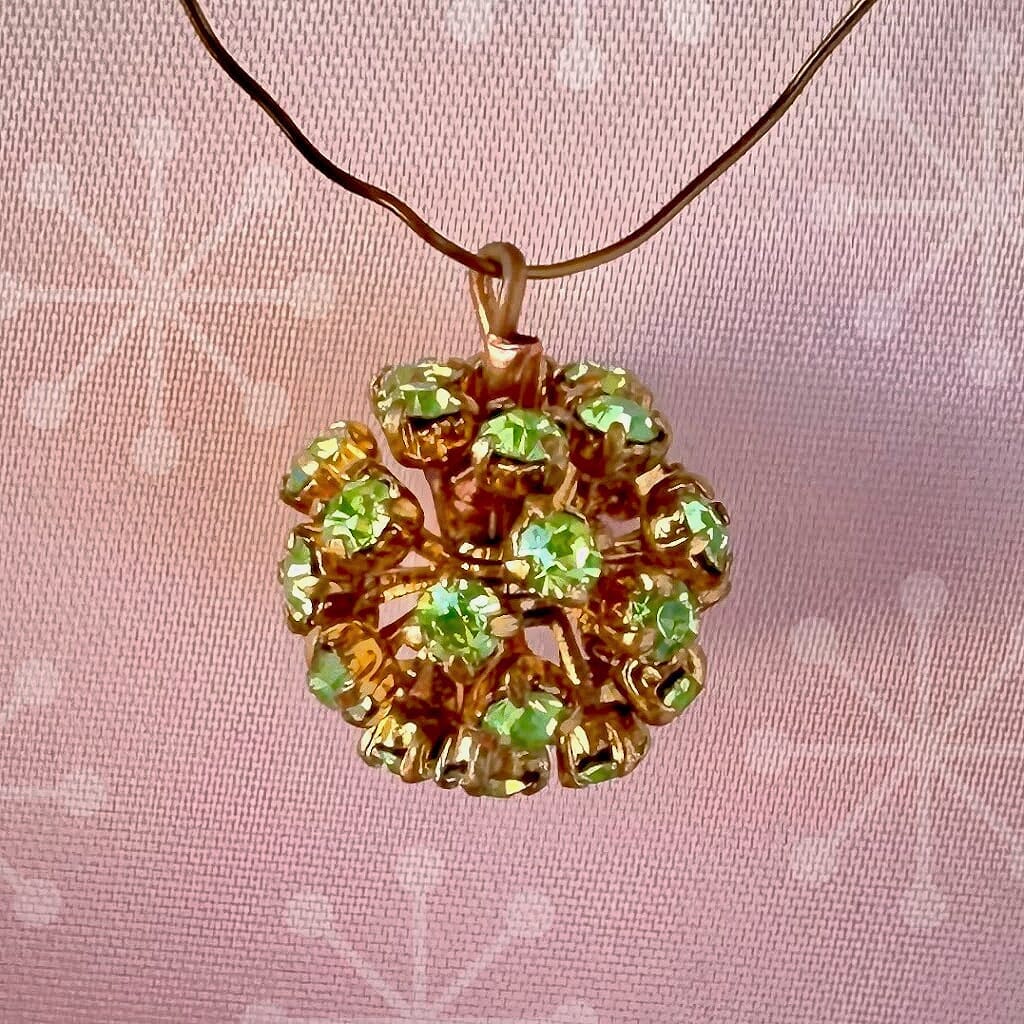 Vintage, Swarovski rhinestone bead ball, peridot-coloured stones and gold toned metal, on a pink background.