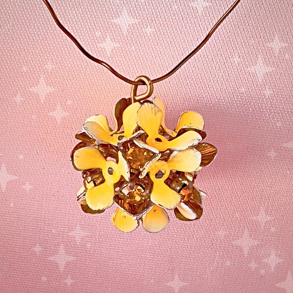 Vintage, Swarovski rhinestone, flower-style bead ball charm, with topaz-coloured stones and yellow petals, on a pink background.