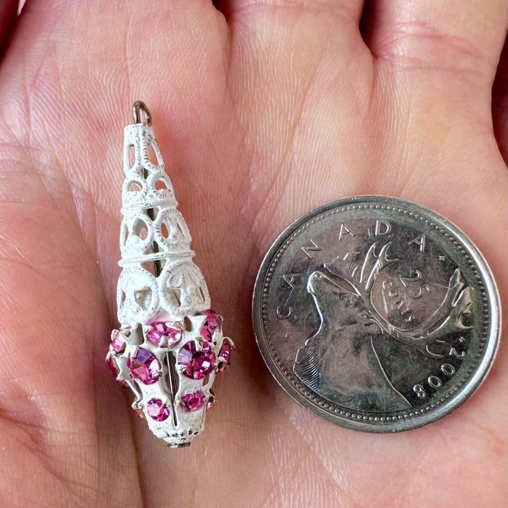 Vintage, Swarovski rhinestone, teardrop-shaped, white filigree bead / charm with rose pink stones on a pink background.