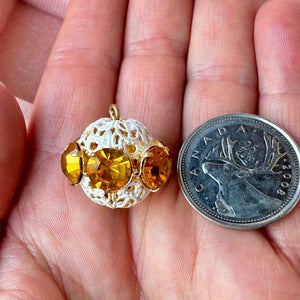 Vintage, topaz-coloured, Swarovski rhinestone bead ball next to a Canadian quarter coin on a hand for size comparison.