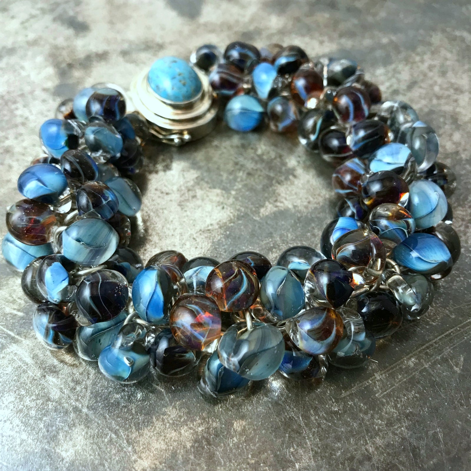 Available at Suzie Q Studio - Handmade glass bead sterling silver charm bracelet. This statement-making charm bracelet was created with a handmade chain of 16 gauge sterling silver rings. Individually handcrafted Unicorne glass teardrop-shaped bead charms are suspended from the chain by smaller sterling silver rings. The finishing touch is a custom made, sterling silver box clasp.